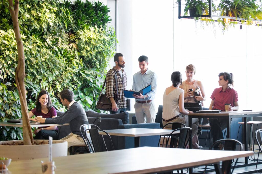 Several people are standing in a bright, modern room and talking. One wall is completely overgrown with green plants, the other side of the wall consists of a large window.